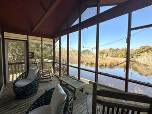 A covered outdoor seating area with wicker furniture and a view of a water body and surrounding vegetation.