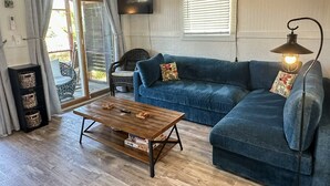 Ein gemütliches Wohnzimmer mit einem blauen Sofa, einem Holztisch, einem Korbstuhl und einem an der Wand befestigten Fernseher.
