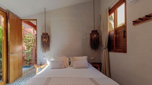Ein Schlafzimmer mit einem großen Bett, zwei Pendelleuchten, einer Holztür und Blick ins Grüne.