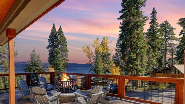 Eine Terrasse mit Sitzgelegenheiten und einem Feuerkorb mit Blick auf einen Wald und ein Gewässer.