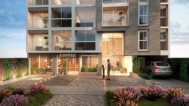 Un bâtiment moderne avec un café au rez-de-chaussée, des balcons et une voiture garée dans l’allée.