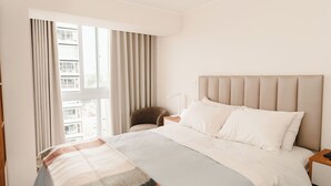 Une chambre d’hôtel avec un grand lit, une table de chevet, une chaise et une fenêtre avec des rideaux.