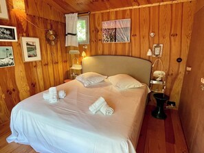 Ein Zimmer mit Holzwänden, einem Bett, zwei Nachttischlampen und einem fenster mit Vorhängen.