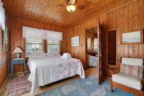 A wooden-paneled room with a bed, a chair, a lamp, and a ceiling fan.