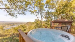 Un bain à remous sur une terrasse offrant une vue sur une rivière et des collines.