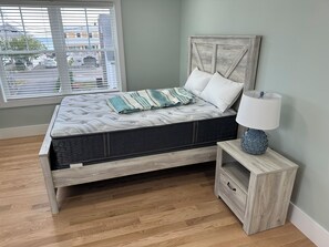 A bedroom with a bed, a nightstand, a lamp, and a window with blinds. - Brand New! Enjoyable 5-bedroom house with AC in Wells Beach (Wells)