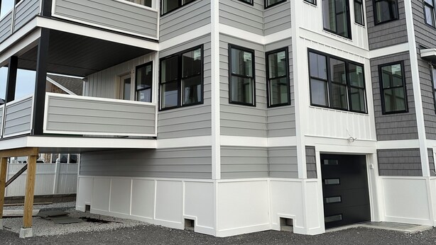 A multi-story residential building with a balcony on the ground floor, large windows, and a flat roof. - Brand New! Enjoyable 5-bedroom house with AC in Wells Beach (Wells)