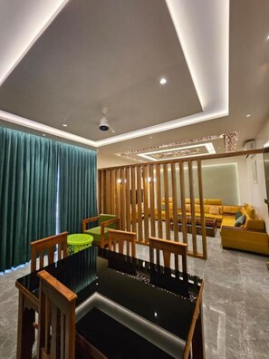 Uma sala de estar moderna com área de jantar, apresentando uma mesa de jantar preta, cadeiras de madeira, um sofá amarelo e uma cortina verde.