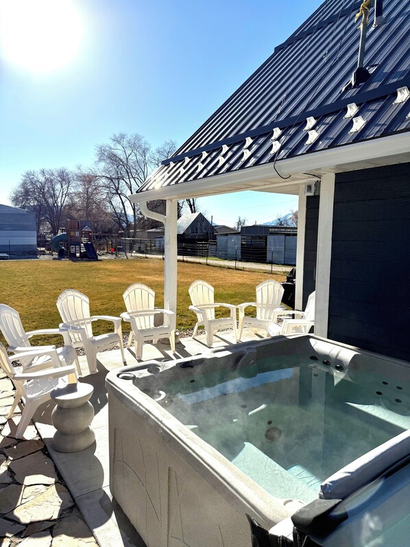 Boblebad med stenskørt, hvide Adirondack-stole og et overdækket område med ståltag.
