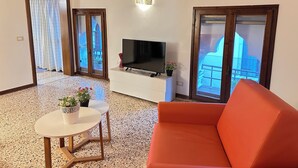 A living room with a TV, a sofa, a small table with a plant, and a balcony with a railing. - Ai Sansoni (Venice)