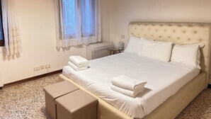 A bedroom with a large bed, a bedside table, a lamp, and a window with curtains. - Ai Sansoni (Venice)