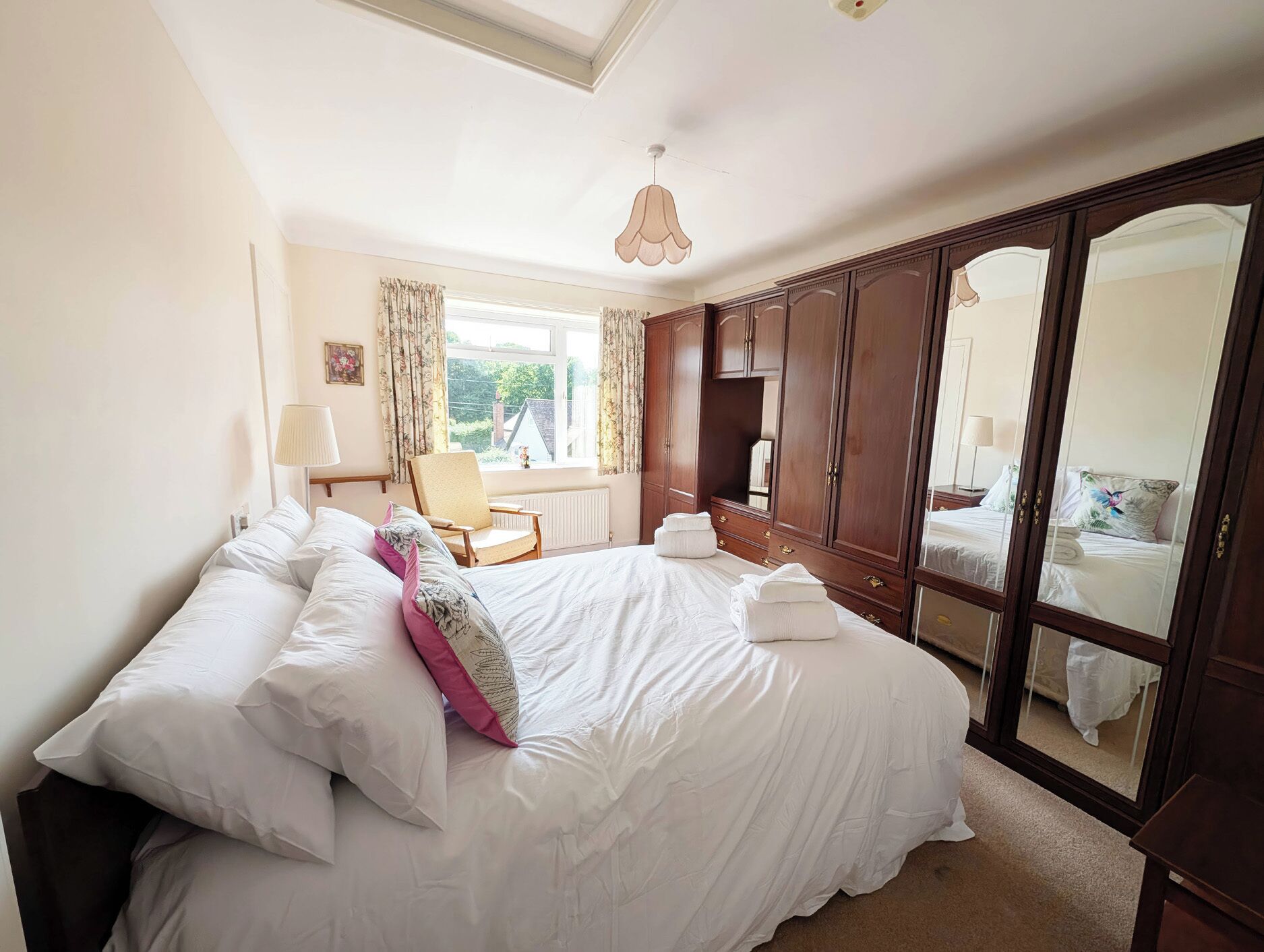 A bedroom with a large bed, a chair, a wardrobe, and a window with curtains.