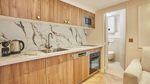 Een kleine keuken met houten kastjes, een marmeren achterwand, een inbouwmagnetron en een vaatwasser.