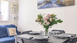 A dining area with a table set for four, a vase of flowers, and a beach-themed painting on the wall. - The Little House with Its Palm Tree (Dolus-d'Oléron)