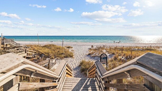 En strand med träpromenader som leder ner till stranden, en sandstrand och havet.