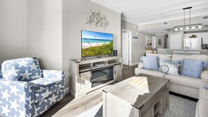Ein modernes Wohnzimmer mit Flachbildfernseher, einer Couch, einem Couchtisch und einer Küche im Hintergrund.