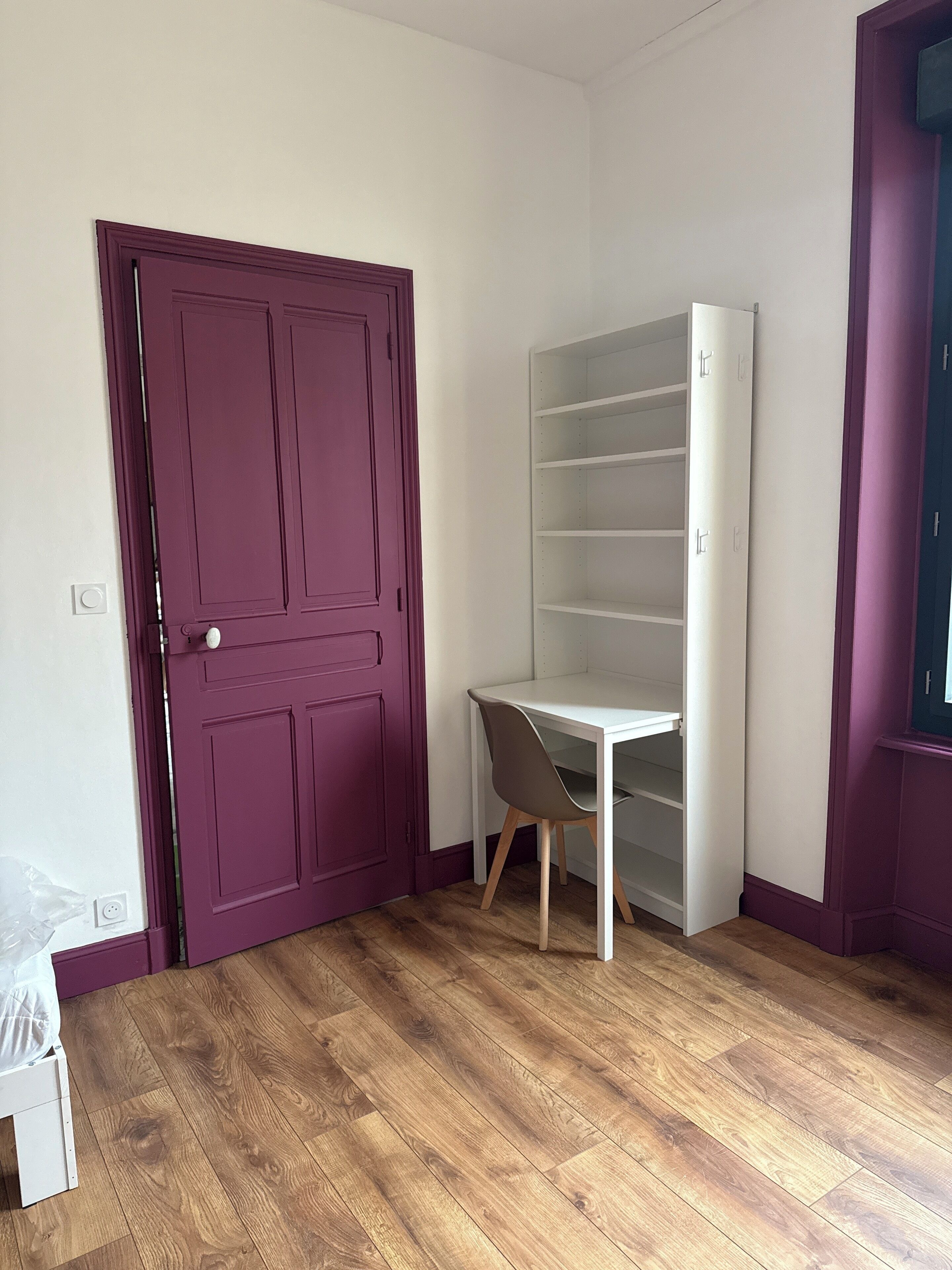 Ein Zimmer mit einer lilafarbenen Tür, einem weißen Schreibtisch und einem Bücherregal.
