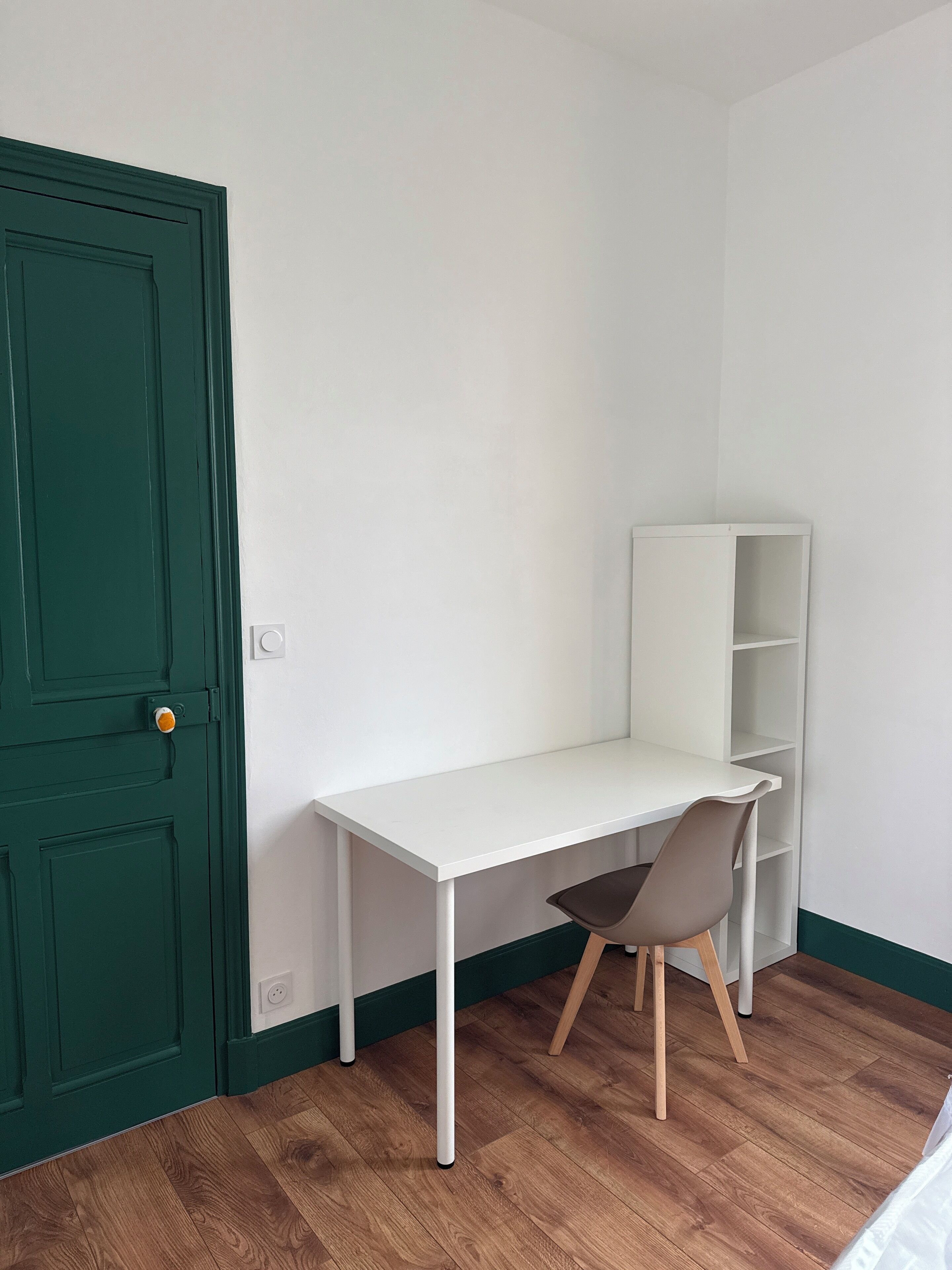 Une pièce avec un bureau blanc, une chaise marron, une porte verte et une étagère blanche.