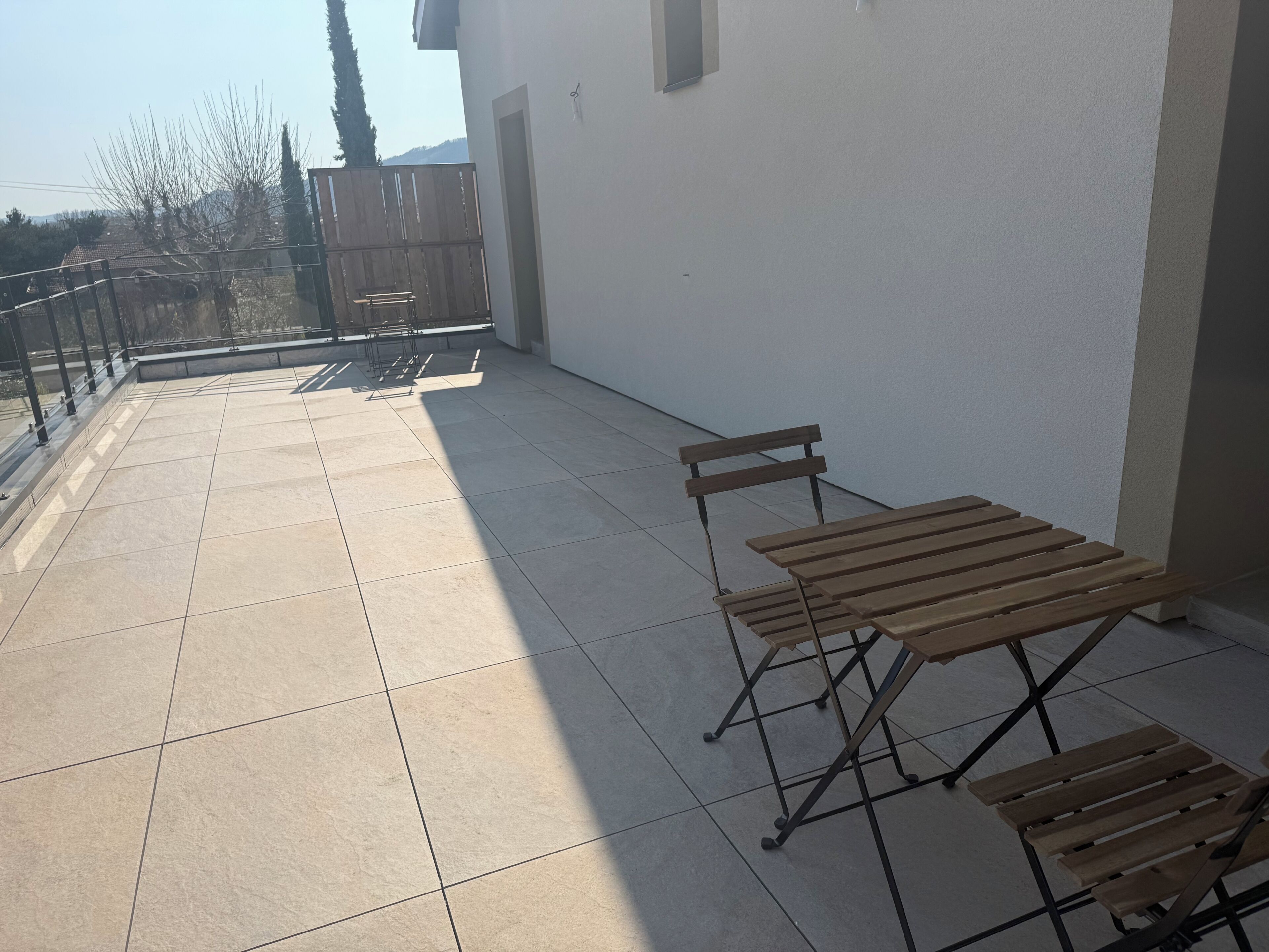 Un balcón con suelo de baldosas, una mesa de madera y un banco.