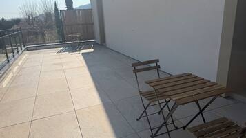 Un balcón con suelo de baldosas, una mesa de madera y un banco.