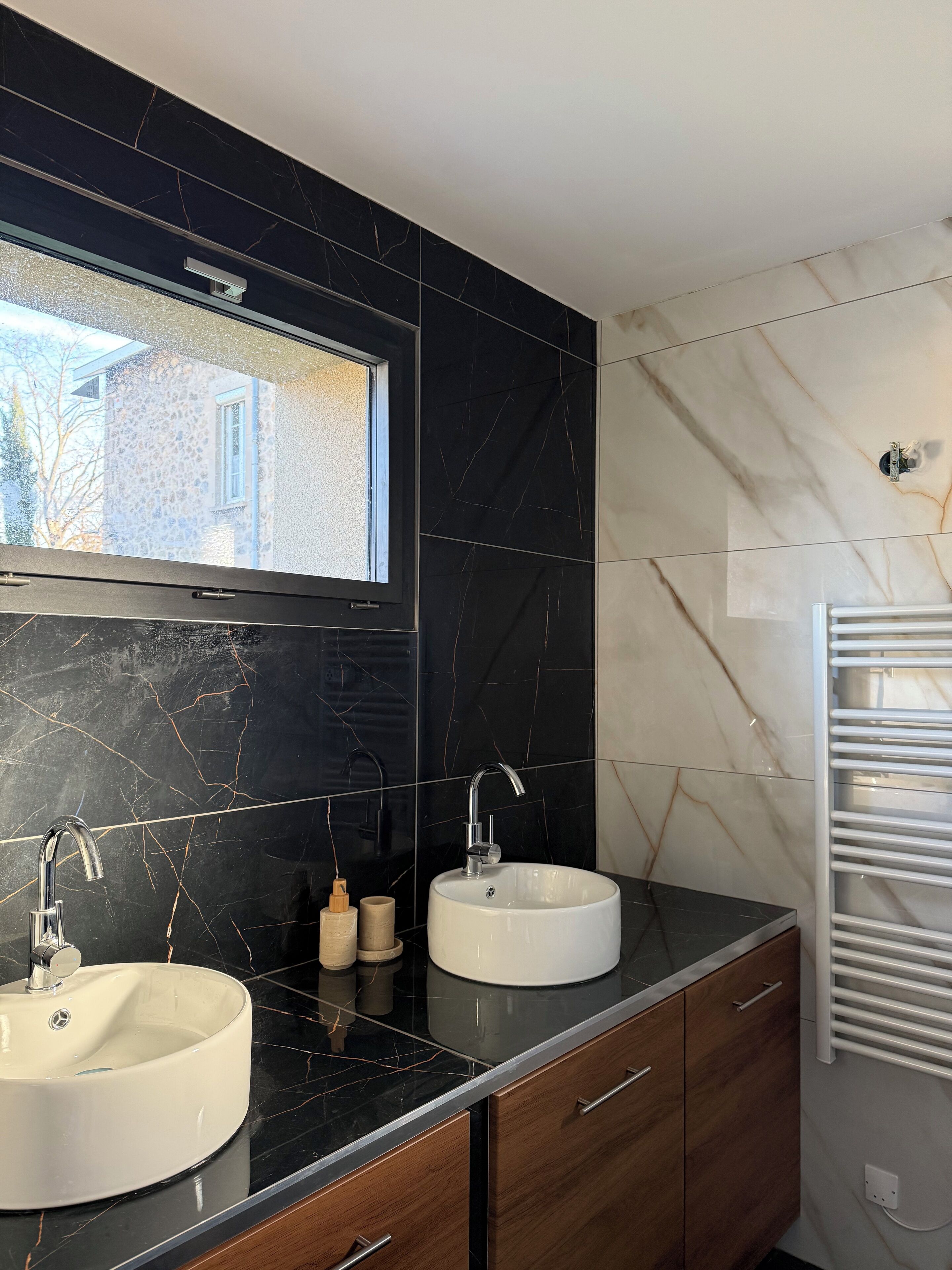 Een moderne badkamer met twee wasbakken, een raam en een handdoekhouder.
