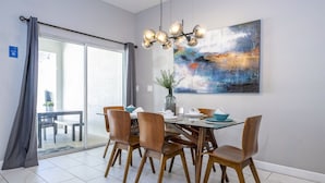 Un comedor con una mesa de vidrio, sillas de madera, una lámpara moderna y un cuadro abstracto de gran tamaño en la pared.