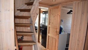 Un escalier en bois mène à une pièce où se trouvent un réfrigérateur noir, des placards en bois et un coin repas visible au fond.