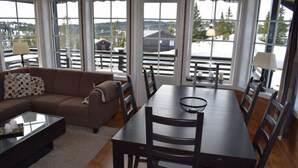Un coin repas avec une table et des chaises en bois foncé, une table basse en verre et un canapé agrémenté d’un coussin à pois. De grandes fenêtres offrent une vue sur l’extérieur.