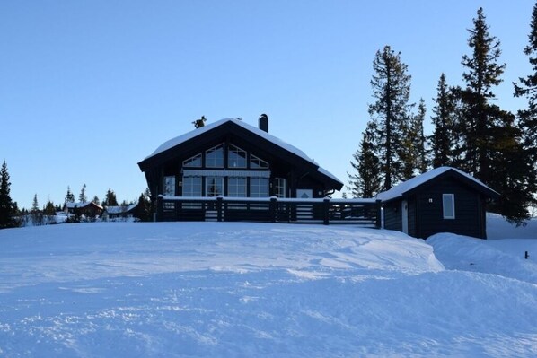A large lodge with a prominent entrance and a smaller cabin nearby, surrounded by snow and trees.