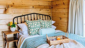 Habitación de cabaña de madera con una cama, un mesita de noche, una lámpara y una cesta con naranjas.
