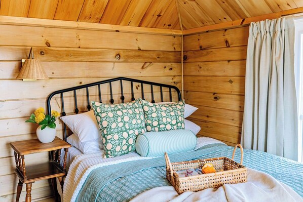 Une chambre rustique en bois, avec un lit, une table de chevet, une lampe et un panier rempli d’oranges.