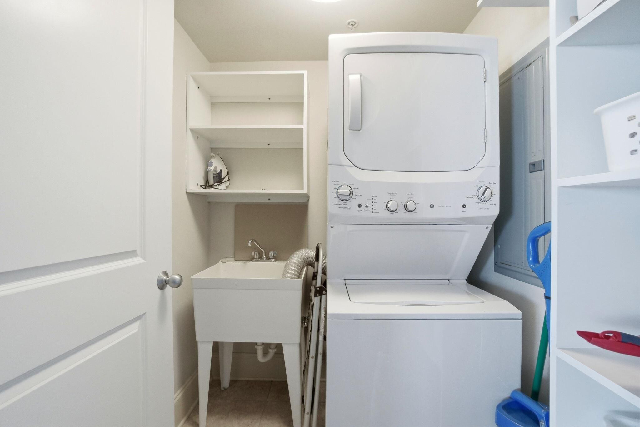 Un cuarto de lavado con lavadora, lavamanos y estanterías.