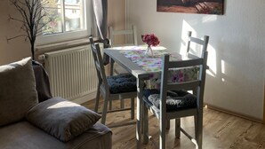 A dining area with a table, chairs, a painting, and a window. - Holiday Apartment by the Zschopau River (Niederwiesa)