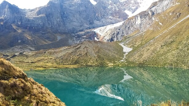 Eine gebirgige Landschaft mit einem klaren See, der die umliegenden Berggipfel spiegelt.