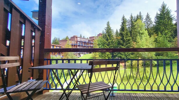Eine Holzterrasse mit Tisch und Bank, mit Blick auf einen gepflegten Rasen und Gebäude im Hintergrund.