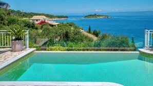 A swimming pool with a stone border, surrounded by greenery and overlooking a coastal view. - Villa Avgerini Paxos I: Deluxe beachfront apartment with breathtaking sea views (Gaios)