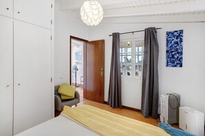 A bedroom with a bed, a chair, a radiator, and a window with curtains. - Holiday Home 'Sunset Cliffs By Slice Of Heaven' with Sea View, Private Terrace and Wi-Fi (Ribeira Brava)