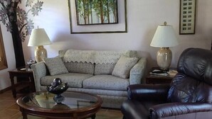 A living room with a sofa, a coffee table, a leather armchair, a floor lamp, and a wall-mounted picture frame. - Tropical paradise getaway on the Treasure Coast -FL- (Jensen Beach)