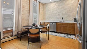 Una cucina compatta con parete in mattoni, mobili in legno, un tavolo rotondo con sedie e un'ampia finestra con tende.