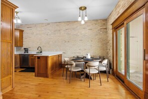 A kitchen with wooden cabinets, a central island with chairs, and a dining table. - Marina View | River Street Lofts | Lake Michigan (Elk Rapids)