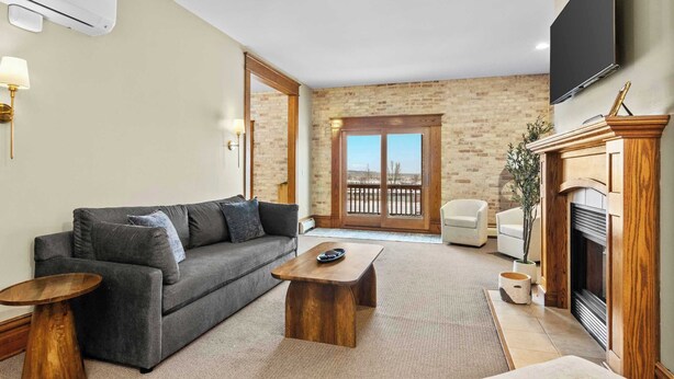 Ein Wohnzimmer mit Sofa, Couchtisch, Fernseher, Kamin und Blick durch eine Glastür.