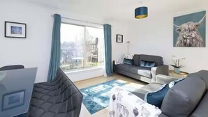 A modern living room with a sofa, a dining table, and a large window with curtains. - Bright 3 Bed Apt overlooking River, SEC & Hydro (Glasgow)