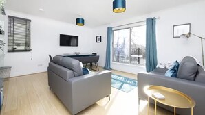 A modern living room with two grey sofas, a small round coffee table, a desk with a chair, and a large window with curtains. - Bright 3 Bed Apt overlooking River, SEC & Hydro (Glasgow)