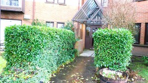 A narrow pathway flanked by well-maintained hedges leading to a dark brown door with a triangular roof. - Bright 3 Bed Apt overlooking River, SEC & Hydro (Glasgow)