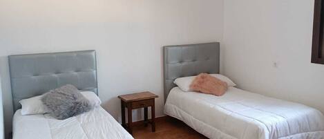 Una habitación con dos camas individuales, una mesita de noche de madera y un equipo de aire acondicionado en la pared.