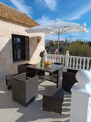 An outdoor patio with wicker furniture, a table with a bowl of fruit, and a white umbrella. - Country House in El Villar   (Fuente Palmera)