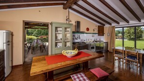 Una cucina con travi in legno, un'area pranzo con tavolo e sedie, e vista su un giardino.