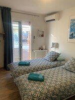 Un dormitorio con cama, una mesita, unidad de aire acondicionado y vistas a través de un ventanal.
