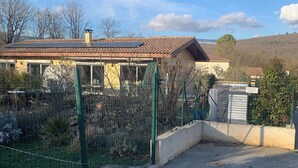 Egy lakóövezet, ahol egy cserépfedeles tetővel és kerítéssel ellátott kerttel rendelkező ház található.