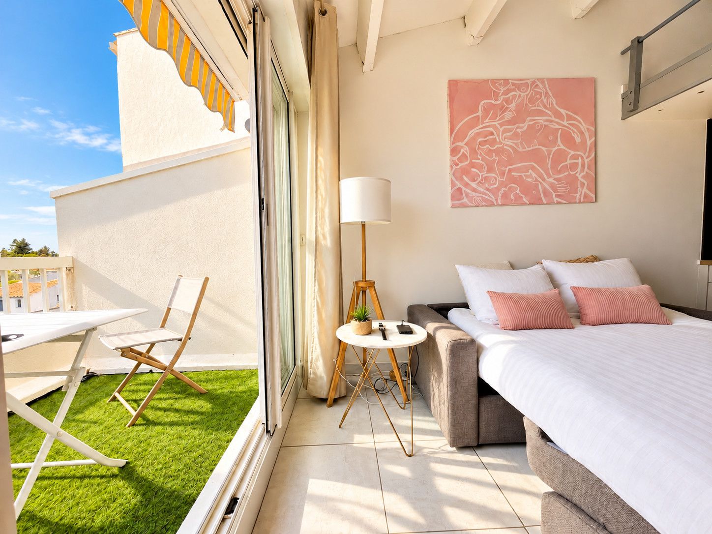 Une chambre moderne avec un lit, une table de chevet et une vue sur un balcon agrémenté d’une chaise et d’une table.